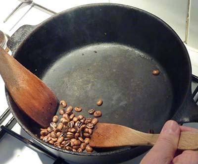 An image of coffee beans being roasted on a stovetop wok